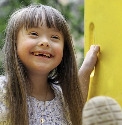 photo of a girl with downs syndrome with a terrific smile playing at a playground
