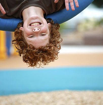 photo of a boy smiling and waving, upside down, on a playground