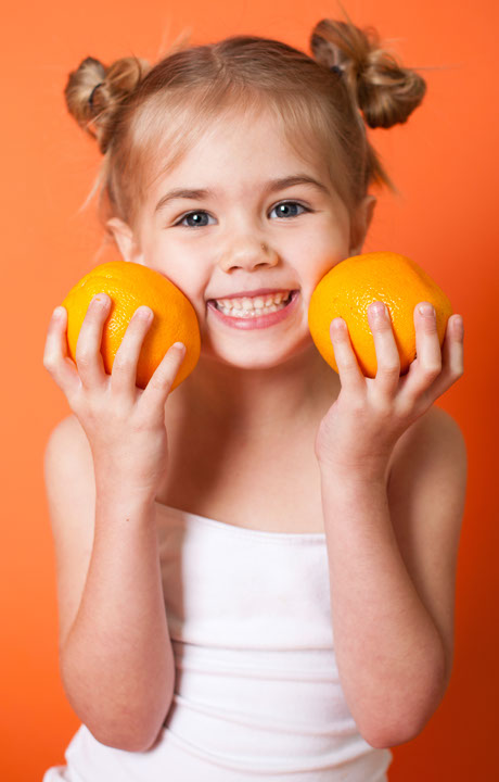 Photo of a smiling girl holding up two oranges