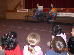 photo of two pediatric dental team members educating a group of children at their school auditorium.